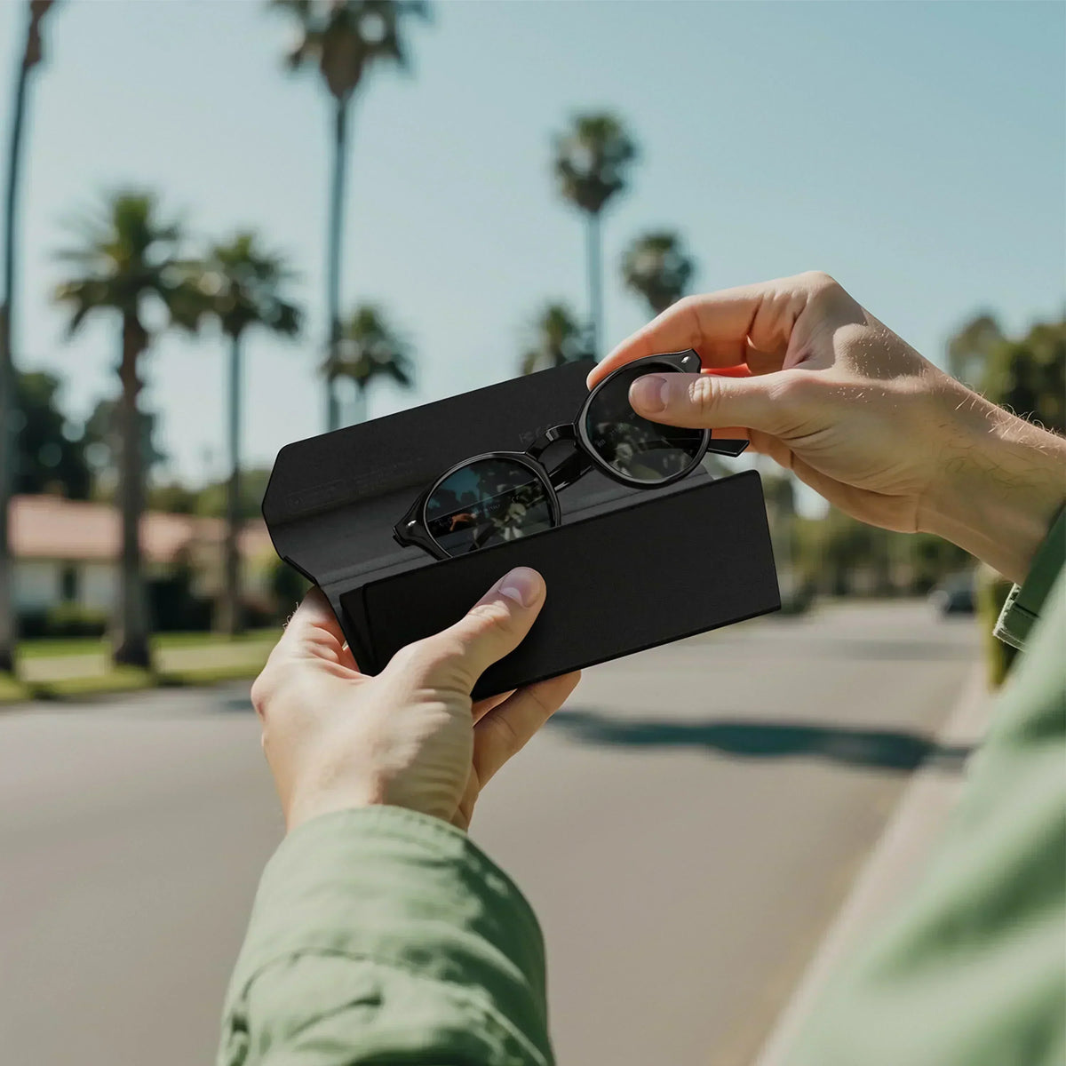 Satechi Vegan-Leather FindAll™ Glasses Case in black, shown open with round folding sunglasses being removed by a person outdoors.