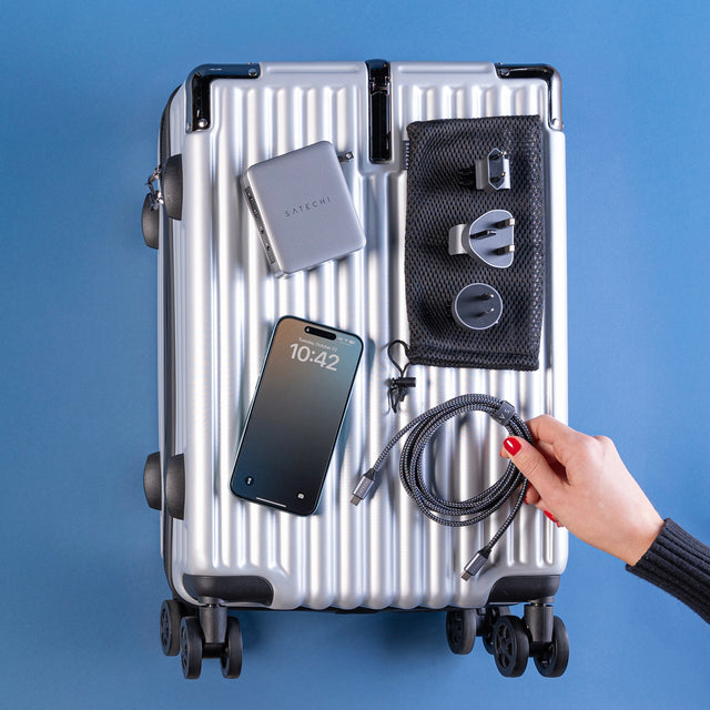 A flat lay showing a 145W USB-C 4-Port GaN Travel Charger with international power outlet options, iPhone, and cable on top of suitcase.