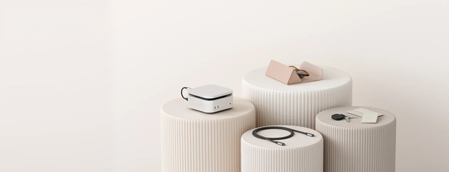Satechi accessories displayed on white fluted pedestals, including a silver desktop charging hub, a pink leather case, a braided USB-C cable, and a key tracker with keys and a card.