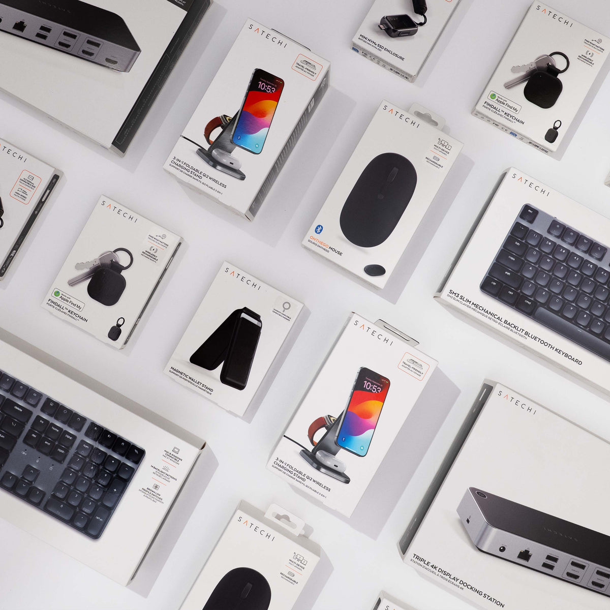 Assortment of Satechi product boxes on a white surface: 3-in-1 Foldable Qi2 Wireless Charging Stand, Mini NVMe SSD Enclosure, Findall Keychain, OnTheGo Mouse, SM3 Slim Mechanical Backlit Bluetooth Keyboard, Magnetic Wallet Stand and Triple 4K Display Docking Station.