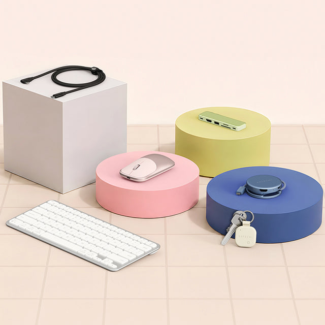 Satechi accessories, USB-C Snap Hub, OntheGo 5-in-1 Multiport adapter, Ex Mouse, and EX1 Keyboard on pastel display blocks. Leaning against block is a sand FindAll keychain tracker on keys.