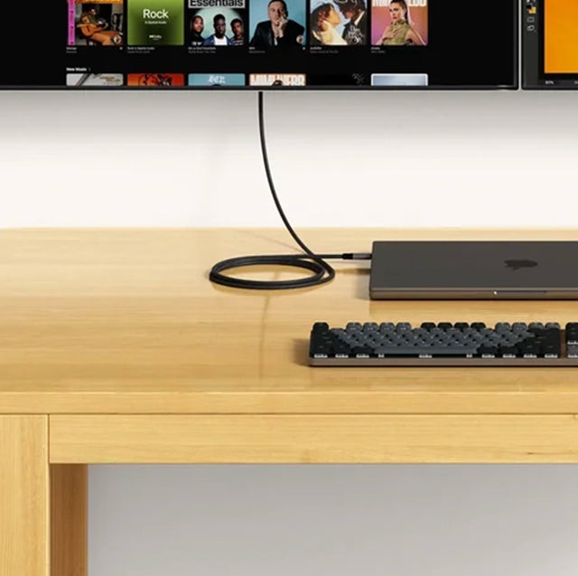 Satechi braided USB-C To HDMI 2.1 8K Cable connecting a laptop to a monitor above a desk with a mechanical keyboard.