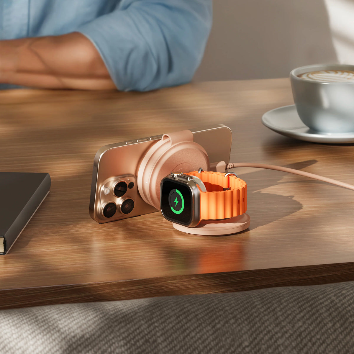 OntheGo 3-in-1 Charger in Desert Rose, folded into a stand on a cafe table, charging an iPhone and an Apple Watch