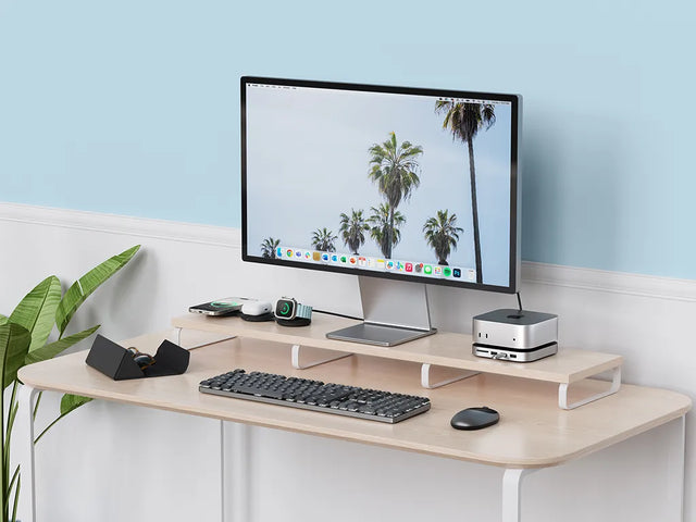 Desk setup with a Mac mini on a Satechi Mac Mini M6/M5 Pro/M4 Stand & Hub with SSD Enclosure, a monitor on a wooden riser shelf, a wireless keyboard and mouse, and OntheGo™ 3-in-1 Charger for iPhone, AirPods and Apple Watch.