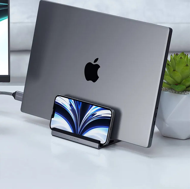 Satechi Dual Vertical Laptop Stand on a white desk, holding a MacBook upright with an iPhone in the front slot.