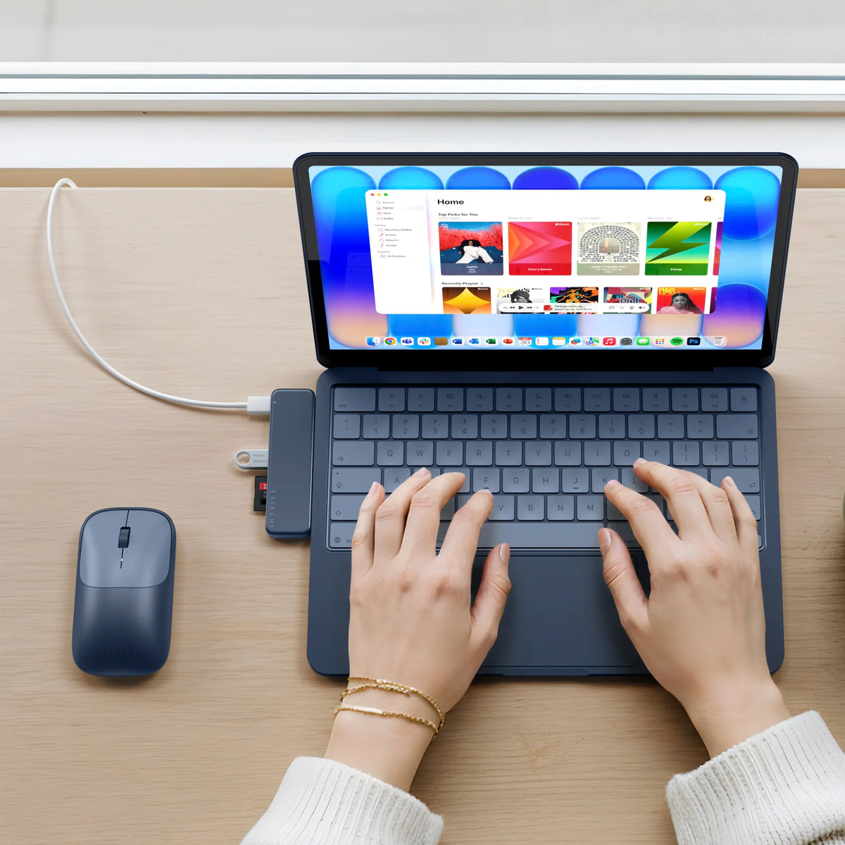 A top-down view of a person using a Indigo MacBook Neo  with a matching USB-C Snap Hub in Indigo and a EX wireless mouse inIndigo on a light wood desk.