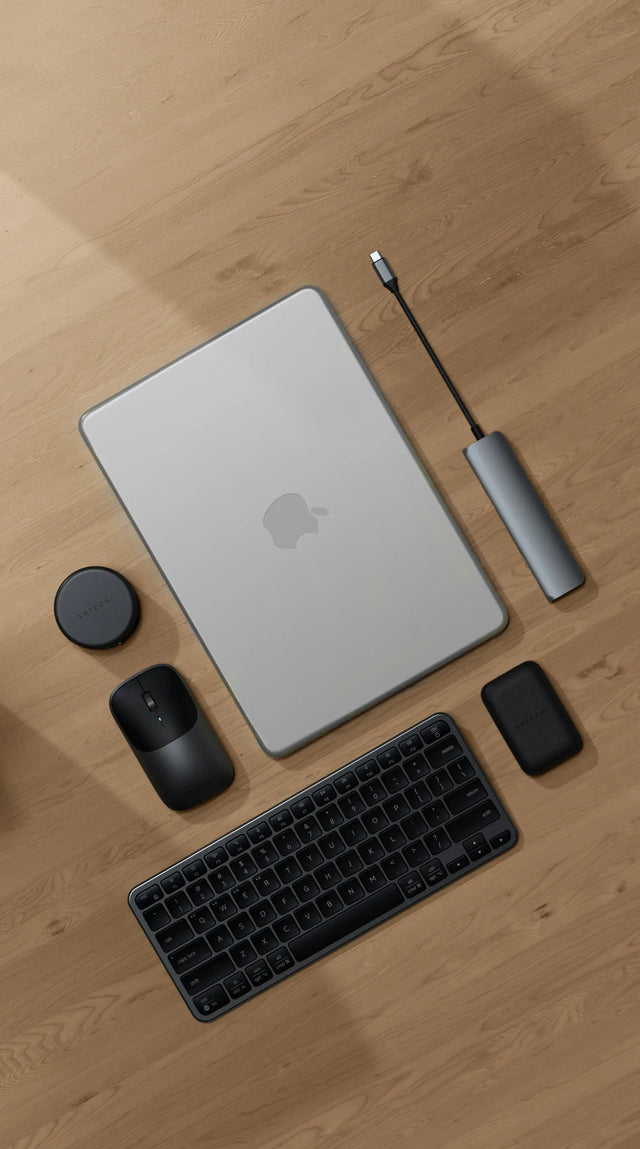 Top-down view of a Satechi workspace featuring a MacBook Air M5 on a light wood floor with a Satechi Slim EX1 Wireless Keyboard in dark, Slim EX Wireless Mouse, 7-in-1 USB-C Slim Multiport Adapter with Ethernet, and OntheGo™ 7-in-1 Multiport Adapter — best MacBook Air M5 accessories 2026
