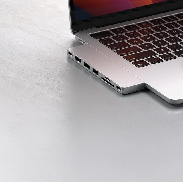 Satechi USB-C hub attached to the side of a silver MacBook, showing HDMI, USB-A, SD and microSD card slots and USB-C ports.