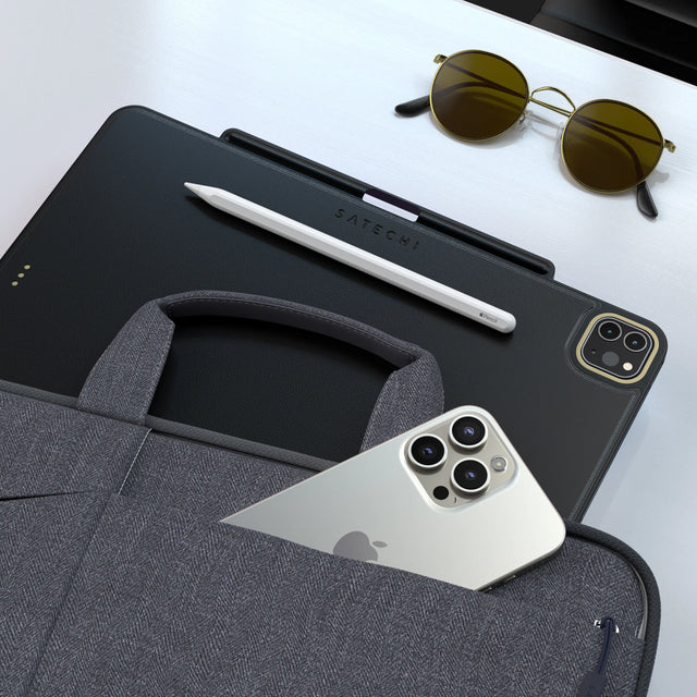 Satechi Vegan Leather Magnetic Case for iPad Pro in black with an Apple Pencil attached, next to an iPhone in a laptop bag pocket and sunglasses.