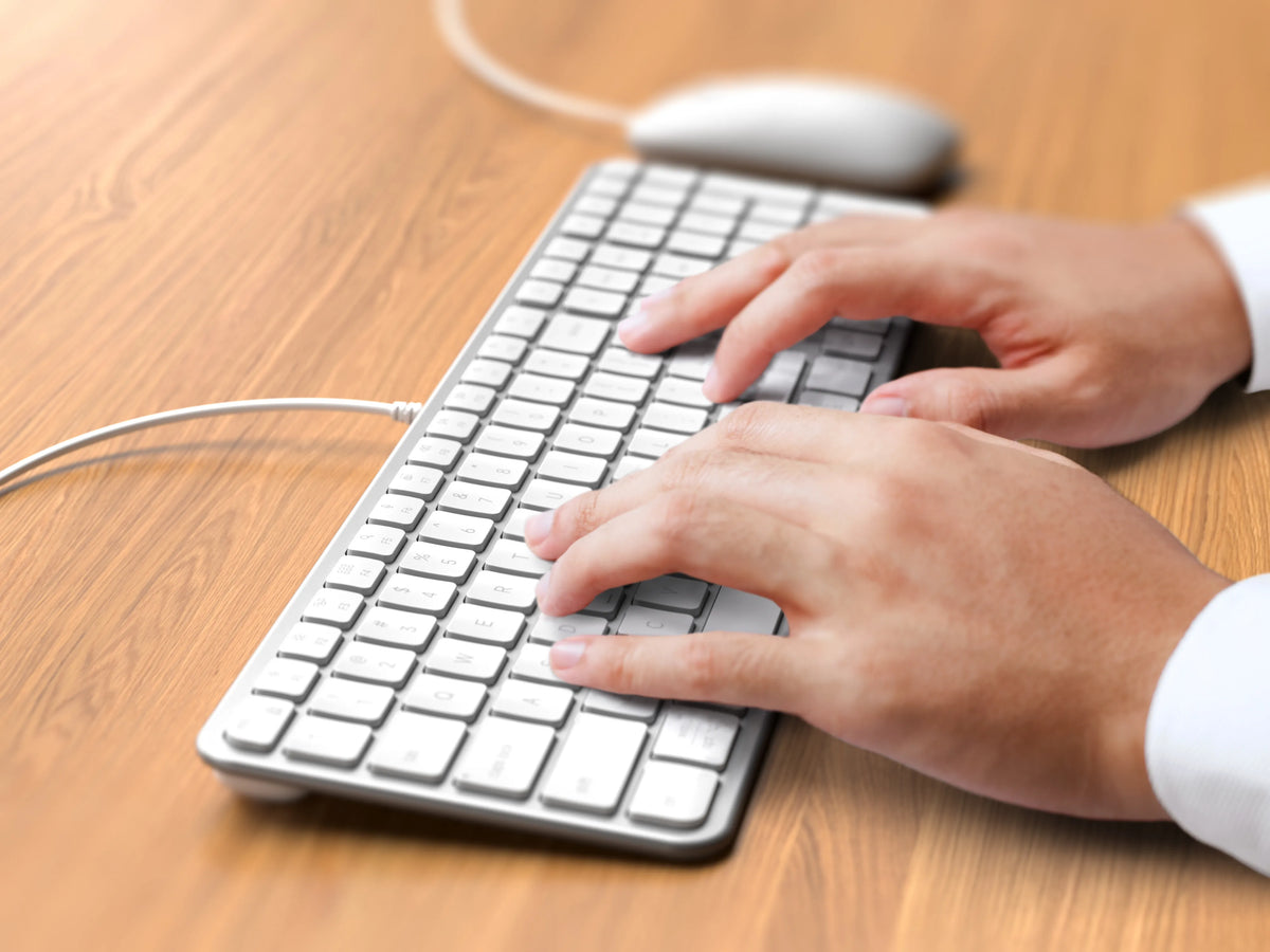 Hands typing on the Slim CLX3 Wired Combo keyboard in Silver on a wooden desk