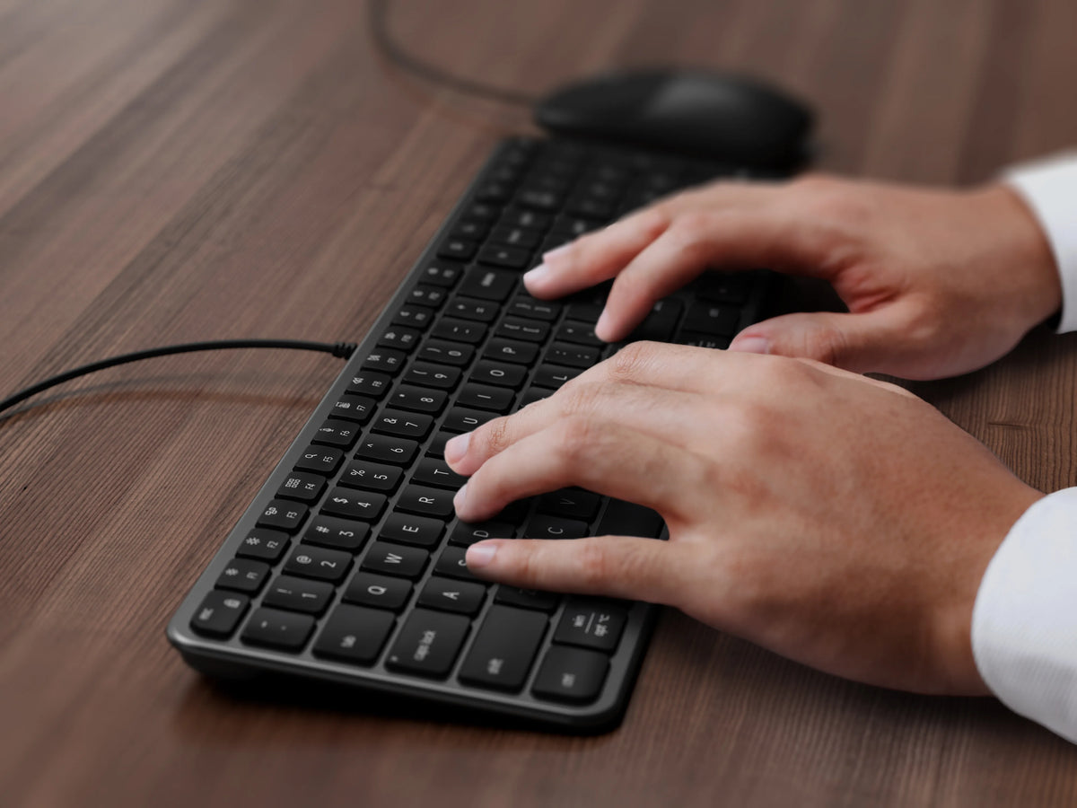 Hands typing on the Slim CLX3 Wired Combo keyboard in Space Black on a wooden desk
