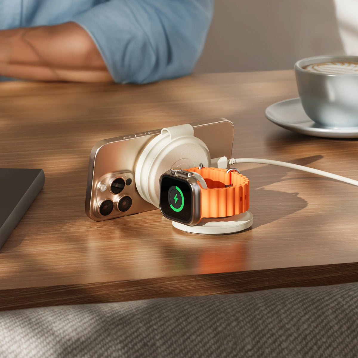 OntheGo 3-in-1 Charger in Sand, folded into a stand on a cafe table, charging an iPhone and an Apple Watch