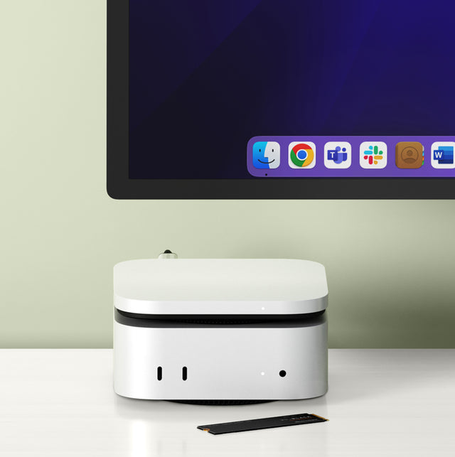 Satechi Mac mini stand and hub with built-in NVMe SSD slot under a silver Mac mini, with an M.2 SSD on the desk below a monitor.