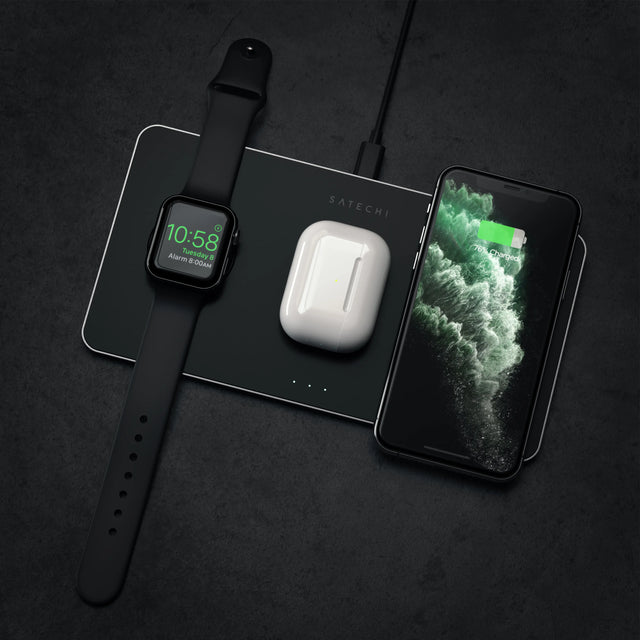 Satechi Trio Wireless Charging Pad charging an Apple Watch, AirPods and an iPhone at the same time on a dark surface.