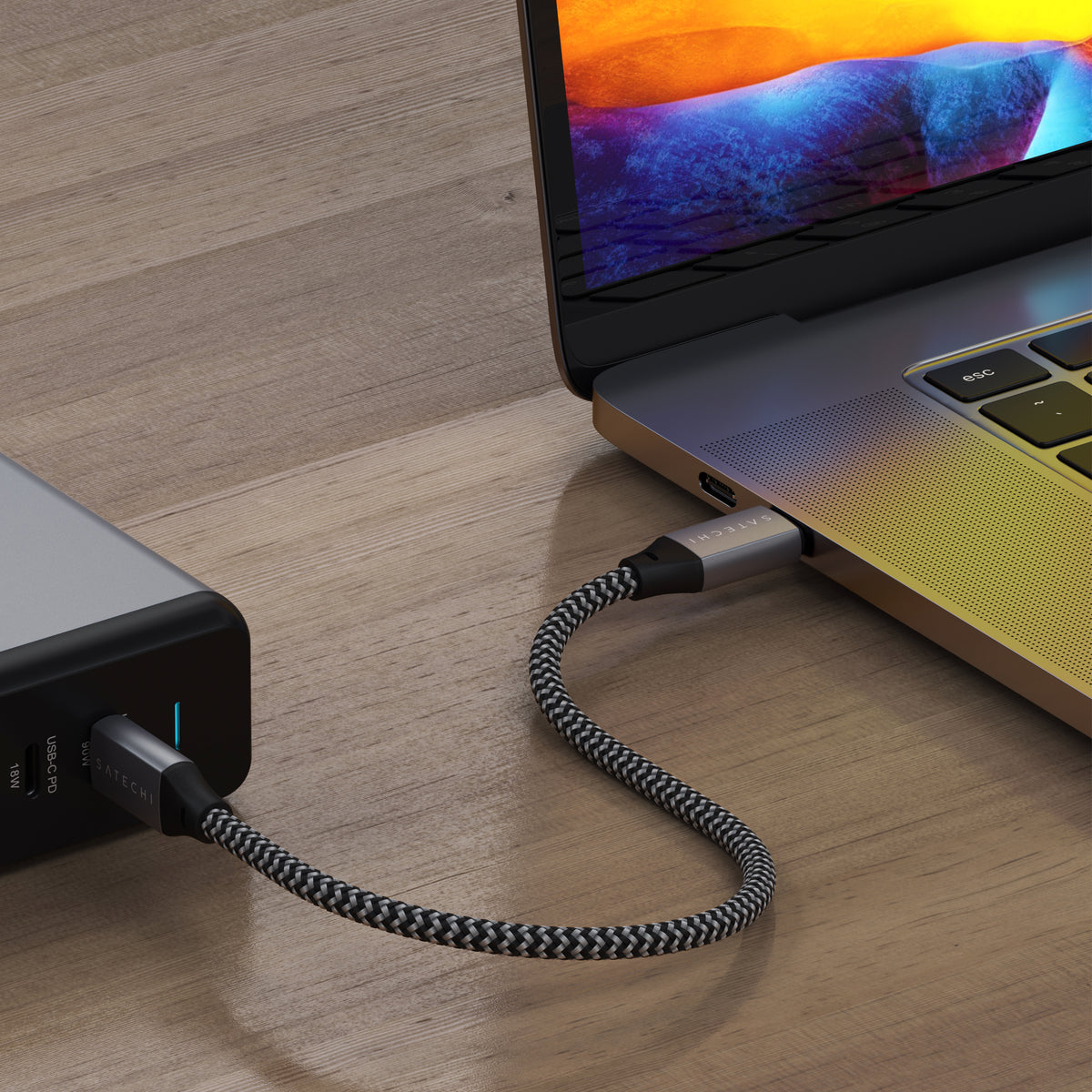 Satechi USB-C to USB-C Cable, 10 inches, braided, connecting a charger to a MacBook on a wooden desk