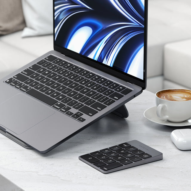 MacBook with a Satechi Aluminum Slim Rechargeable Bluetooth Keypad on a desk with a cup of coffee.