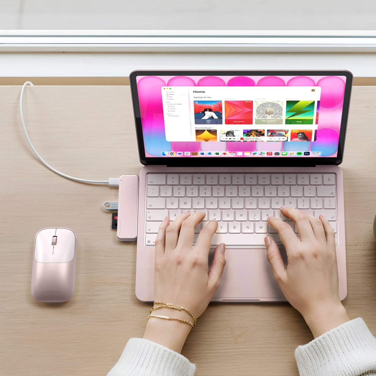 A top-down view of a person using a Blush MacBook Neo  with a matching USB-C Snap Hub in blush and a EX wireless mouse in Blush on a light wood desk.