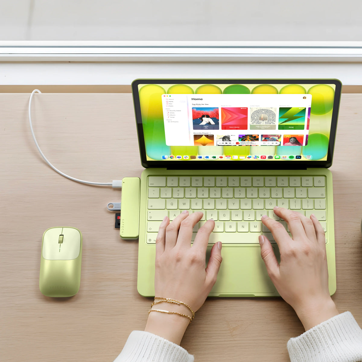 A top-down view of a person typing on a Citrus MacBook Neo with a matching USB-C Snap Hub Citrus and citrus EX mouse. The laptop screen displays colorful content.