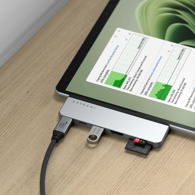 Satechi Dual USB-C Hub for Surface Pro 9 in silver attached to a Surface Pro, with a USB-C cable, USB-A flash drive and microSD card connected while files copy on screen.