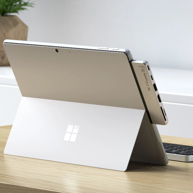 Satechi Dual USB-C Hub attached to the side of a Microsoft Surface Pro 9 on a wooden desk, showing its USB-C, USB-A, HDMI and card reader ports.