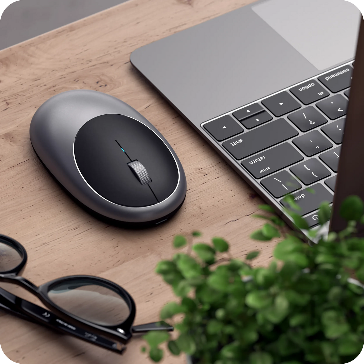 M1 Bluetooth Mouse in Space Gray on a wooden desk next to a laptop and glasses