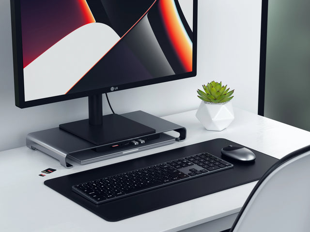 Space gray Satechi USB-C Monitor Stand Hub XL raising an LG monitor on a white desk, with a Satechi keyboard, mouse and desk mat in front.