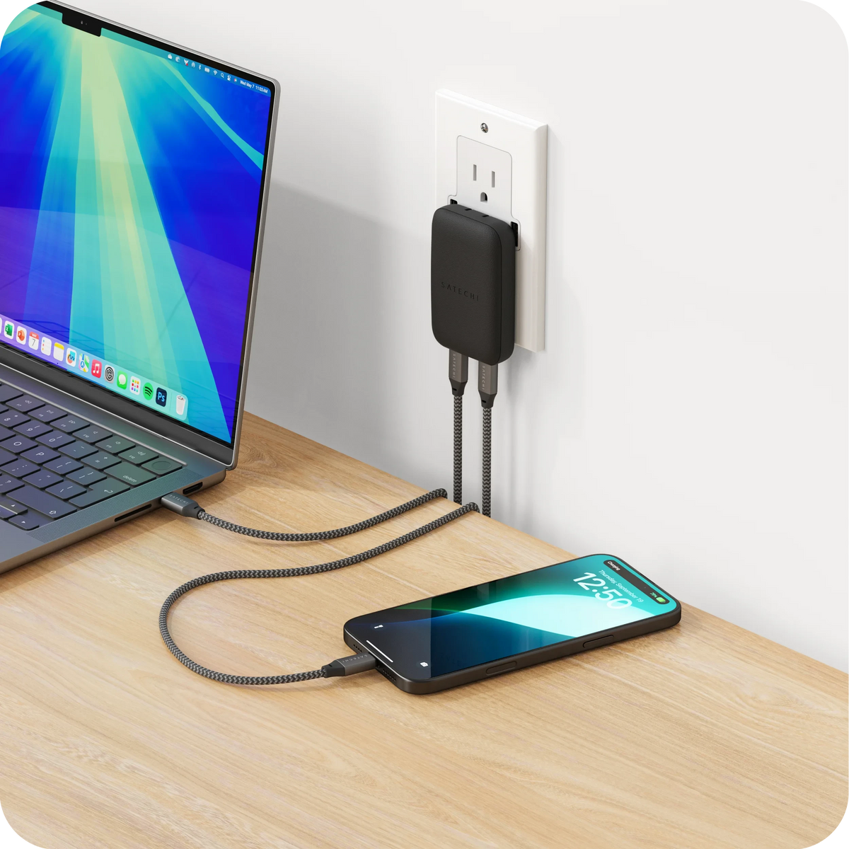 OntheGo 67W Slim Wall Charger in Black plugged into a wall outlet, charging a laptop and an iPhone