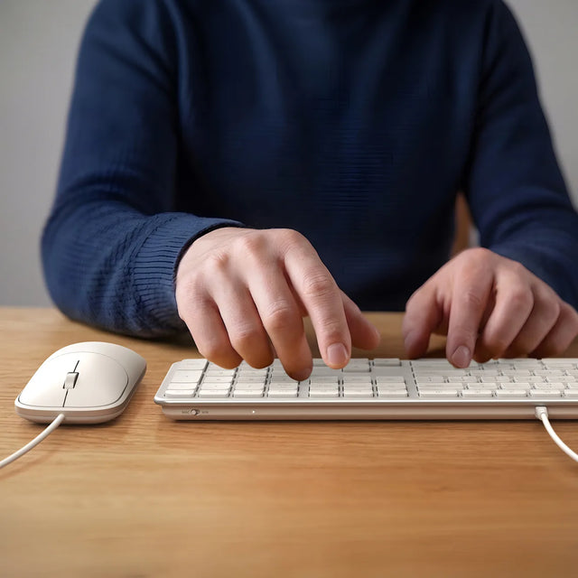 Person typing on the Satechi Slim CLX3 Wired Keyboard in white on a wooden desk, with the matching wired mouse beside it.