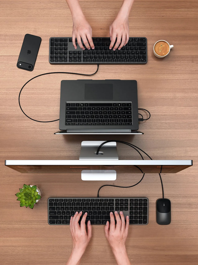 Overhead view of two desks with Satechi Slim CLX3 wired keyboards in use, one connected to a laptop on a stand and one to a monitor, with a wired mouse.