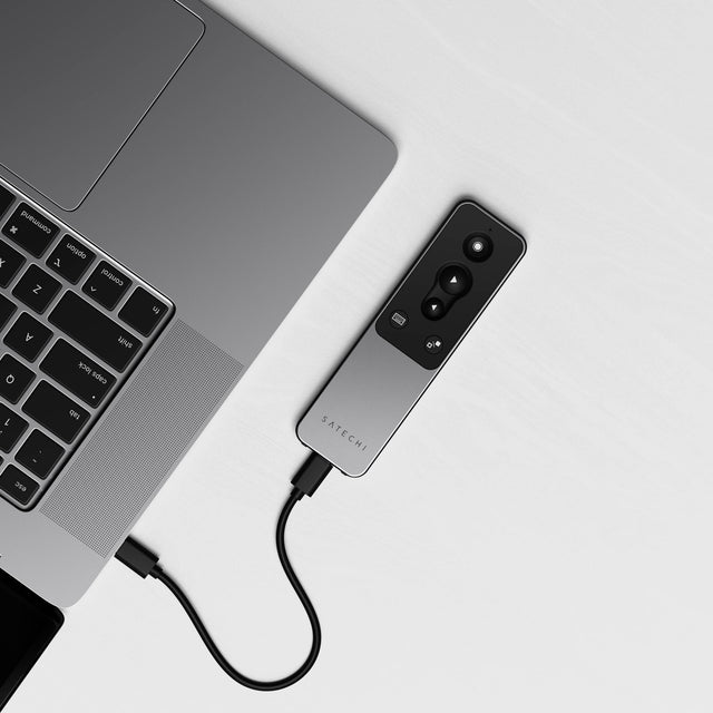 Satechi R1 Bluetooth Presentation Remote charging from a MacBook through a USB-C cable on a white desk.