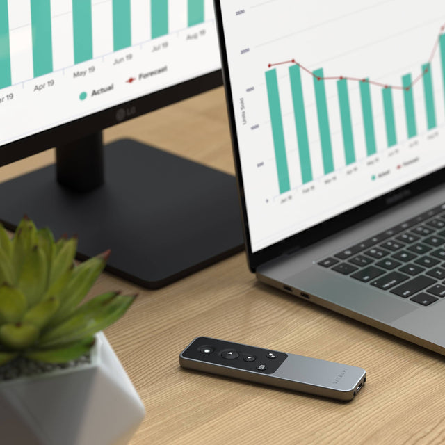 Satechi R1 Bluetooth Presentation Remote on a desk in front of a laptop and monitor showing sales charts.