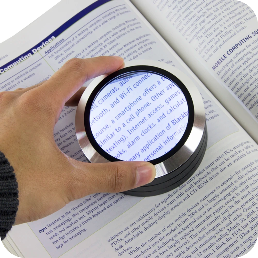 Hand moving the ReadMate LED Desktop Magnifier over a book page to enlarge the text