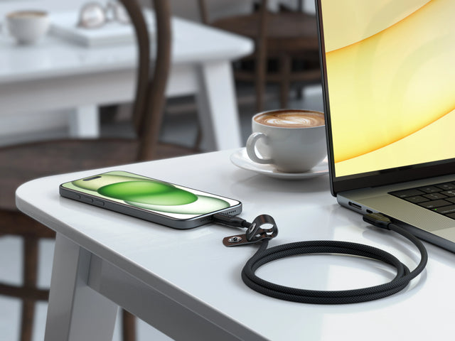 Satechi Right Angle USB-C to USB-C Data and Charge Cable, 1m, connecting an iPhone to a laptop on a cafe table, with its cable strap.