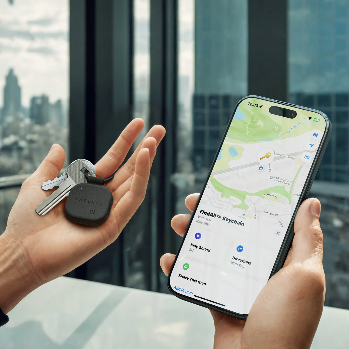 Hand holding keys with the black Satechi FindAll Keychain while the other hand shows its location in the Apple Find My app on an iPhone.