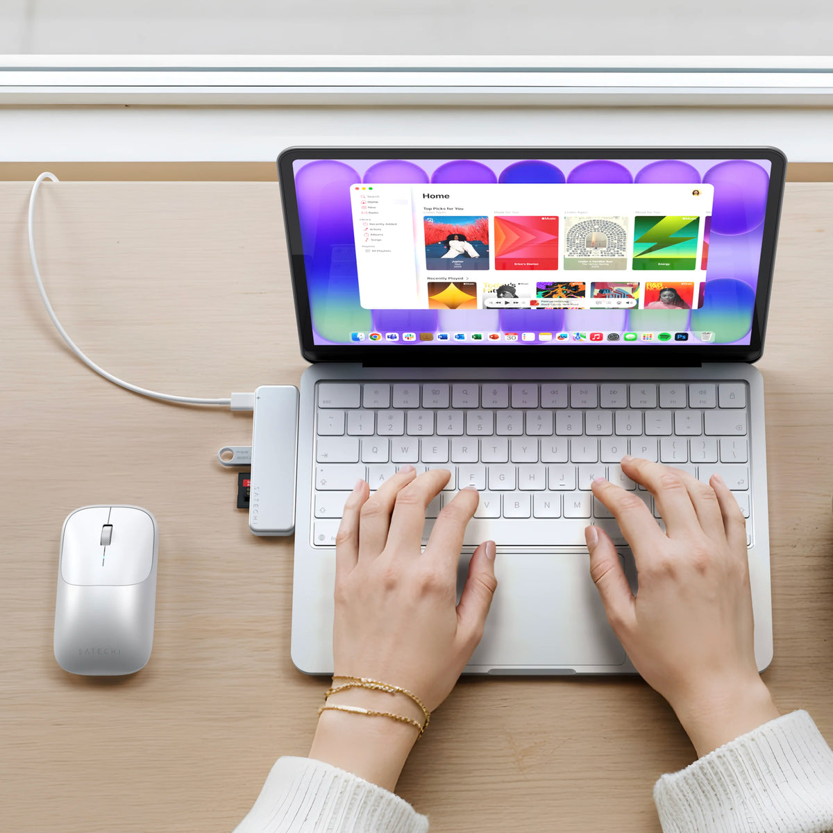 A top-down view of a person using a Silver MacBook Neo  with a matching USB-C Snap Hub in Silver and a EX wireless mouse in Silver on a light wood desk.