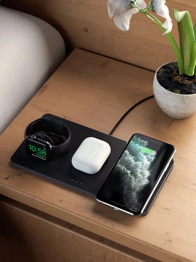 Satechi Trio Wireless Charging Pad on a nightstand charging an Apple Watch, AirPods and an iPhone.