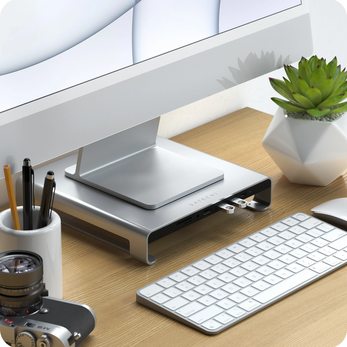 Type-C Aluminum Monitor Stand Hub for iMac in Silver on a wooden desk with a keyboard and camera, close up