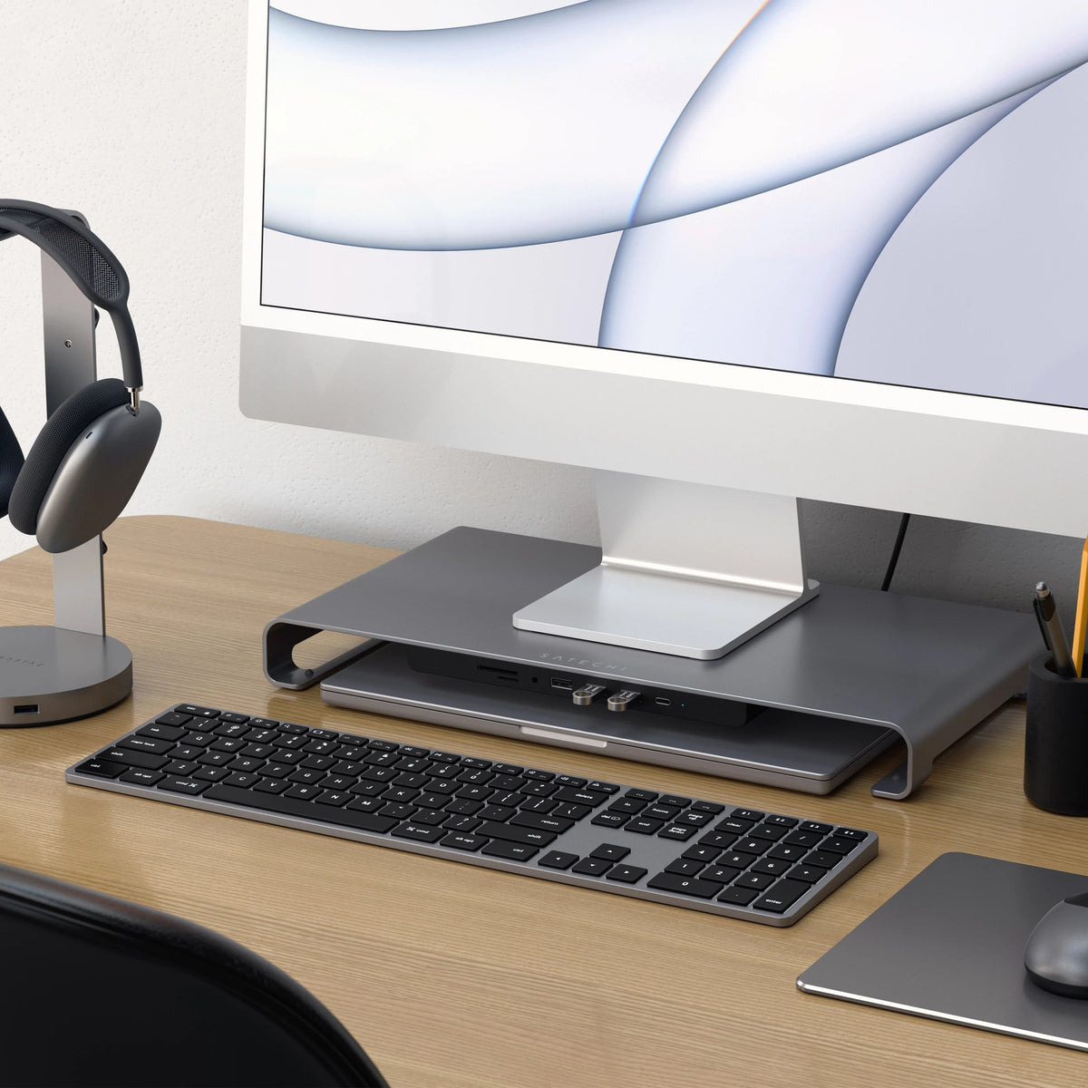 Satechi USB-C Monitor Stand Hub XL under an iMac on a wooden desk, with a keyboard, mouse and headphone stand