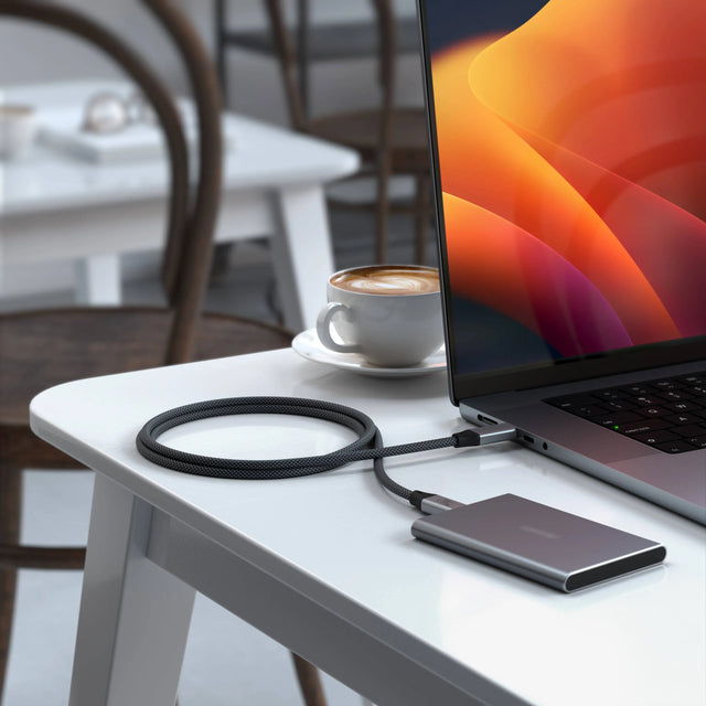 Satechi USB4 Pro Cable connecting a MacBook Pro to an external SSD on a white table.