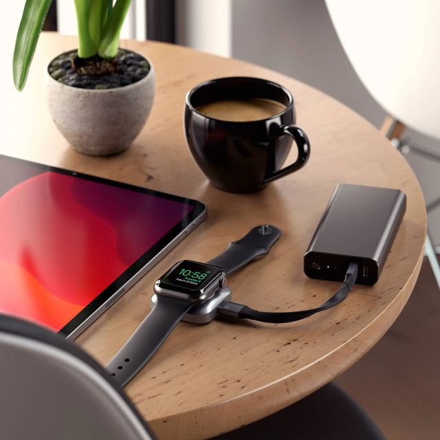 Satechi USB-C Magnetic Charging Dock for Apple Watch plugged into a power bank on a wooden table, charging an Apple Watch.