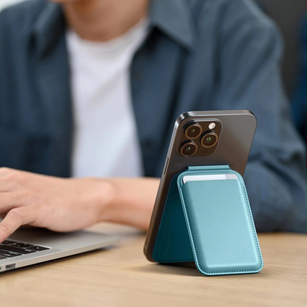 Vegan-Leather Magnetic Wallet Stand in Light Blue propping up an iPhone next to a laptop