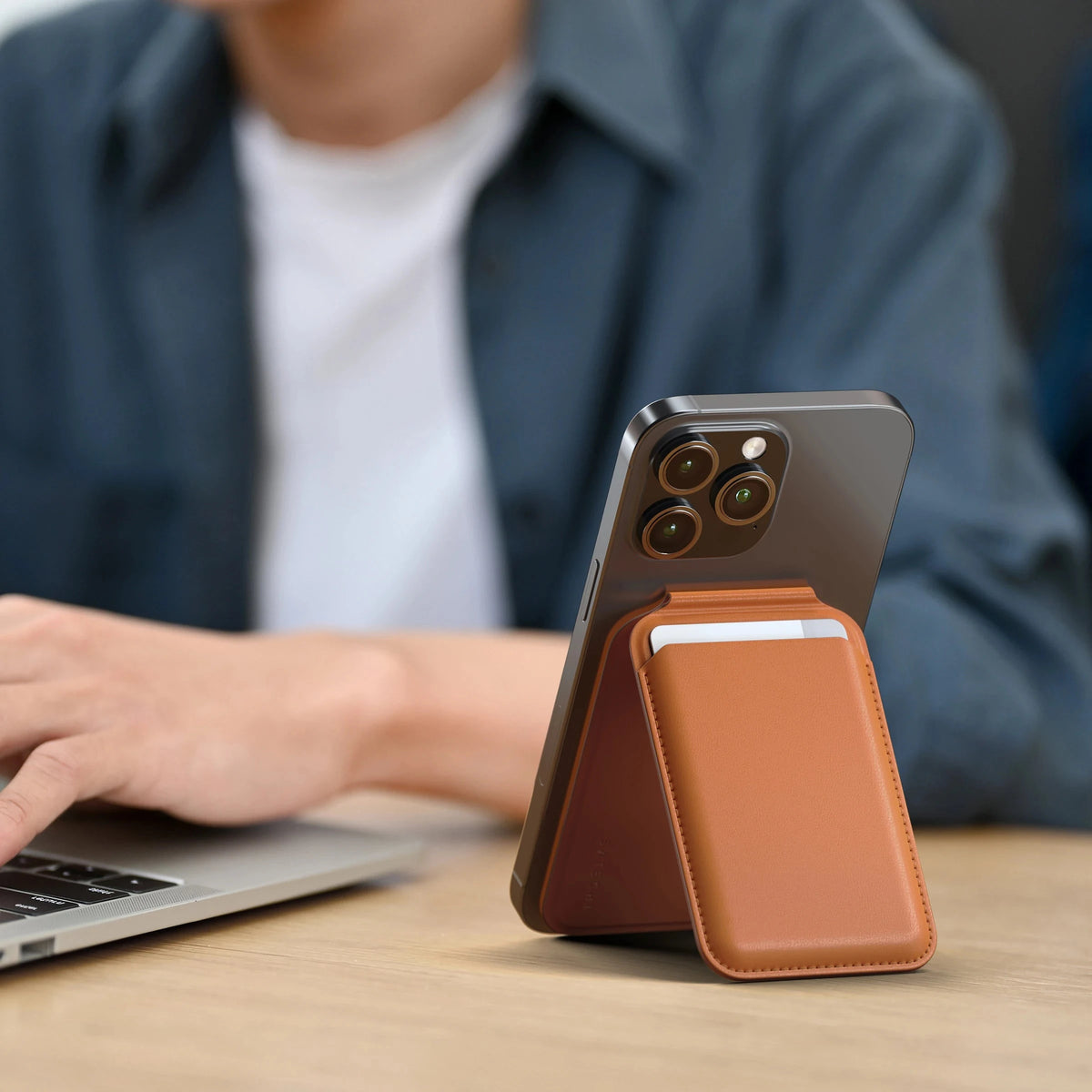 Vegan-Leather Magnetic Wallet Stand in Orange propping up an iPhone next to a laptop
