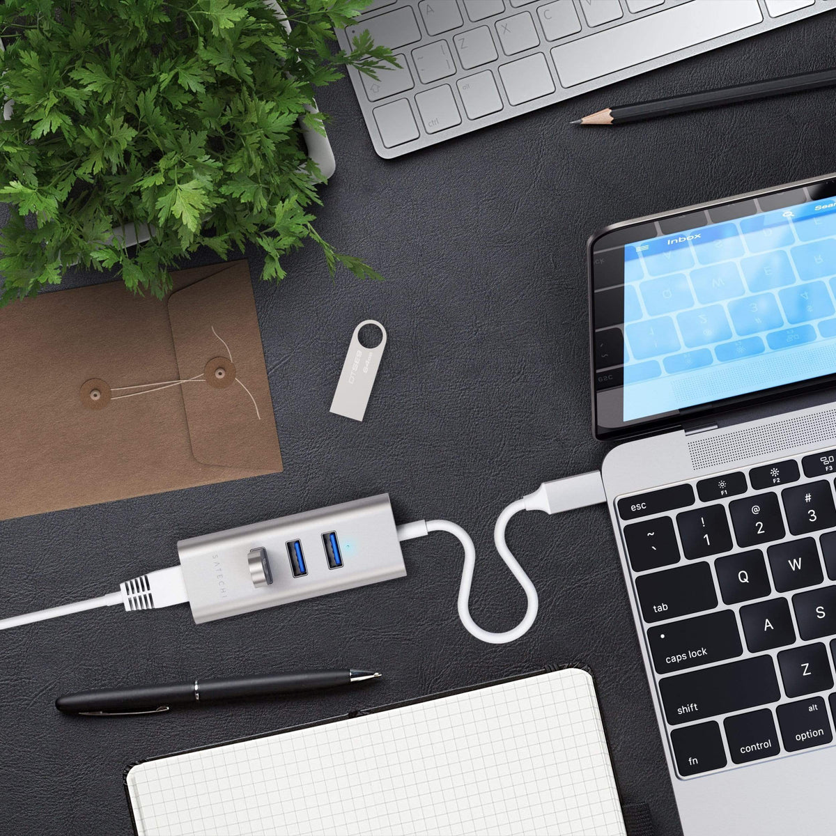 Type-C 2-in-1 USB Hub with Ethernet in Silver plugged into a MacBook on a dark desk with a flash drive, notebook and pen