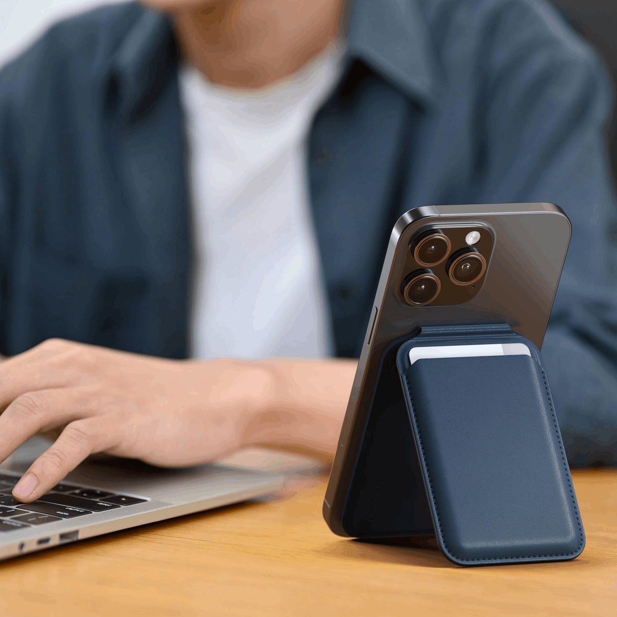 Vegan-Leather Magnetic Wallet Stand in Dark Blue propping up an iPhone next to a laptop